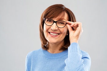 Woman with brown hair and glasses smiling wearing a blue sweater