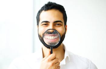 Man smiling through magnifying glass after dental bonding