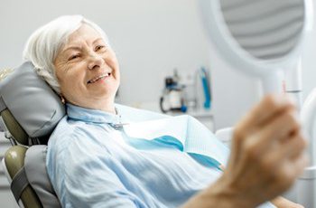 Woman smiling in the dental chair after receiving dental implant supported dentures